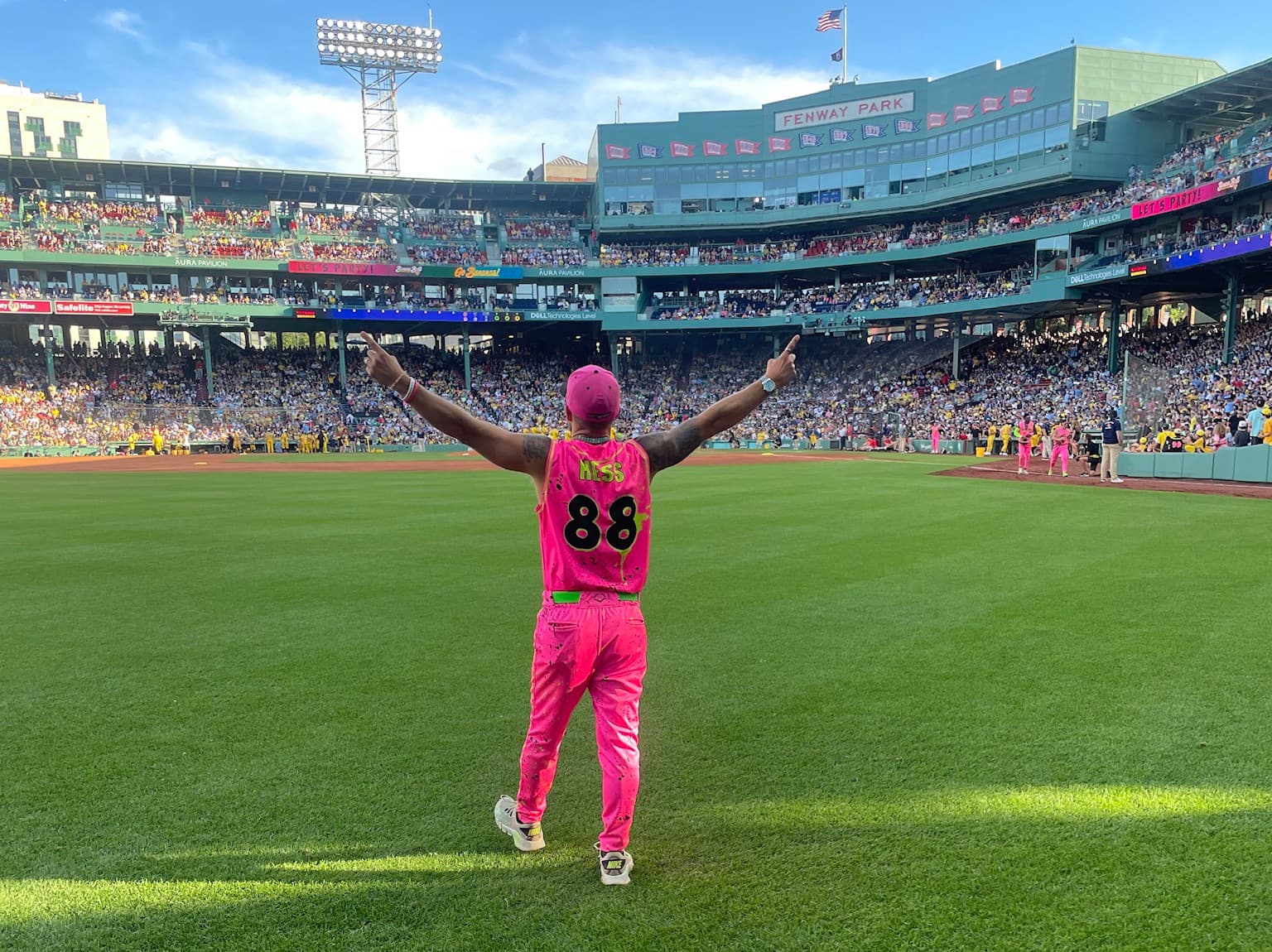 Isaac Hess from behind in his pink number 88 Party Animals uniform, arms raised, facing a sold-out Fenway Park