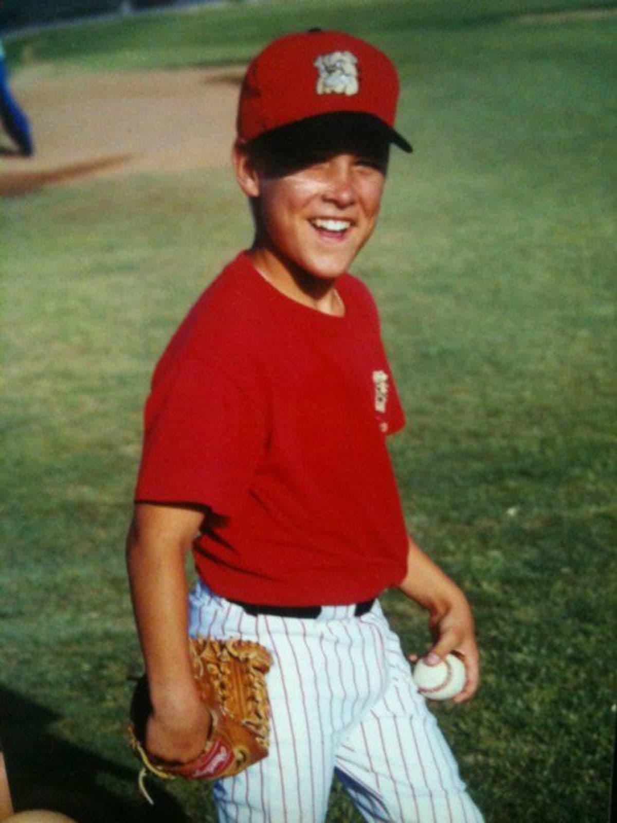 Isaac Hess at about 13, smiling in a red baseball cap and shirt, glove and ball in hand